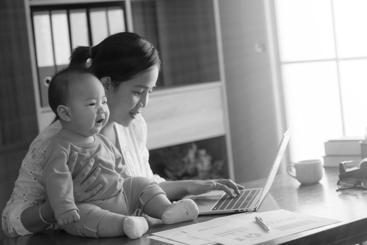 businesswoman mother woman with baby working at the computer. portrait of woman with baby working from home of her online ecommerce shop.technology and lifestyles concept.happy familly and baby theme.